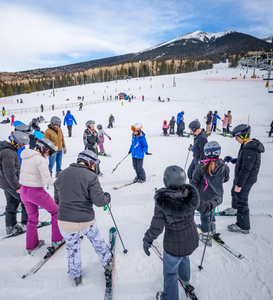 Group of skiers standing in a circle around instructor at Snowbowl