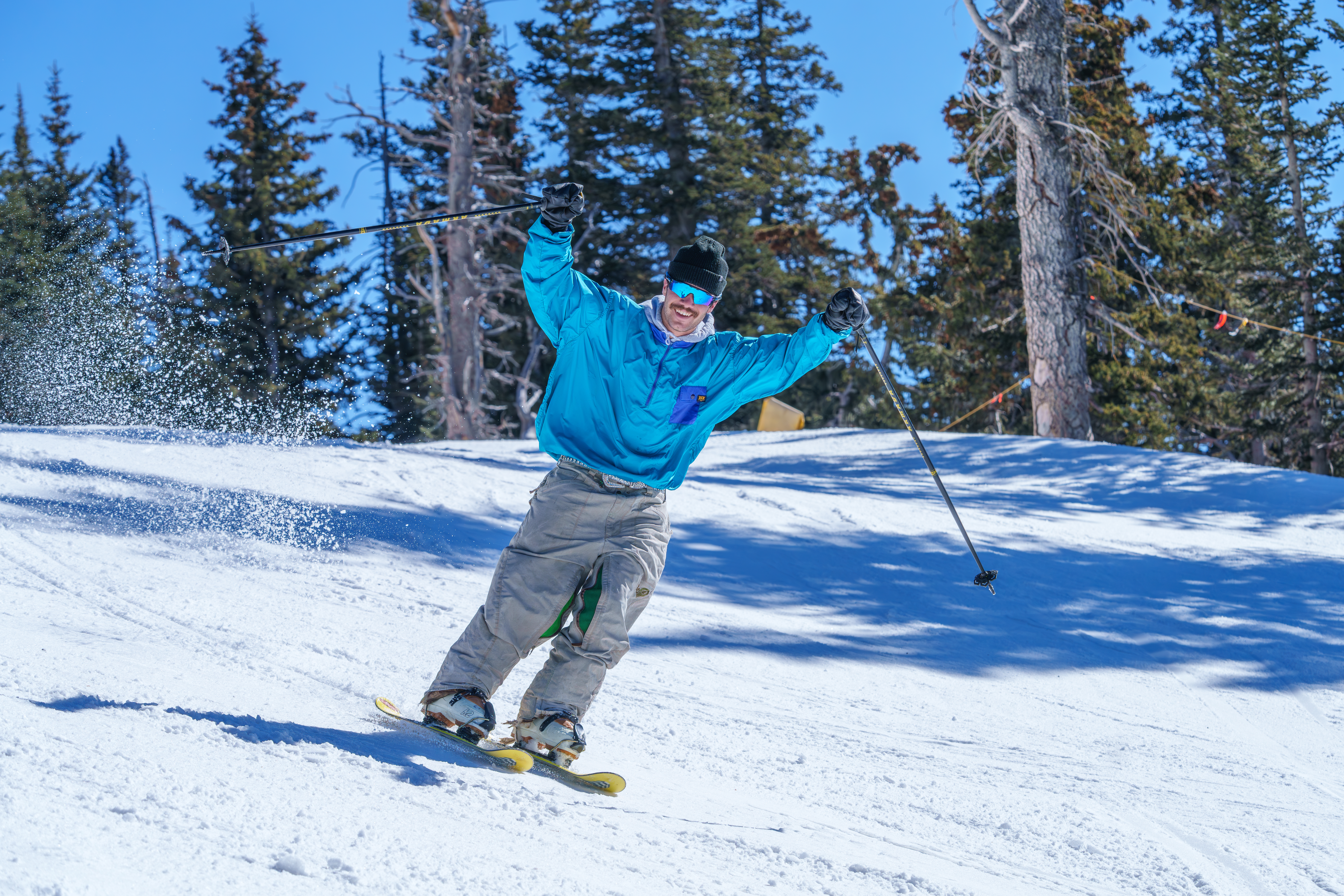 Skier in blue cheering and smiling coming down a run.