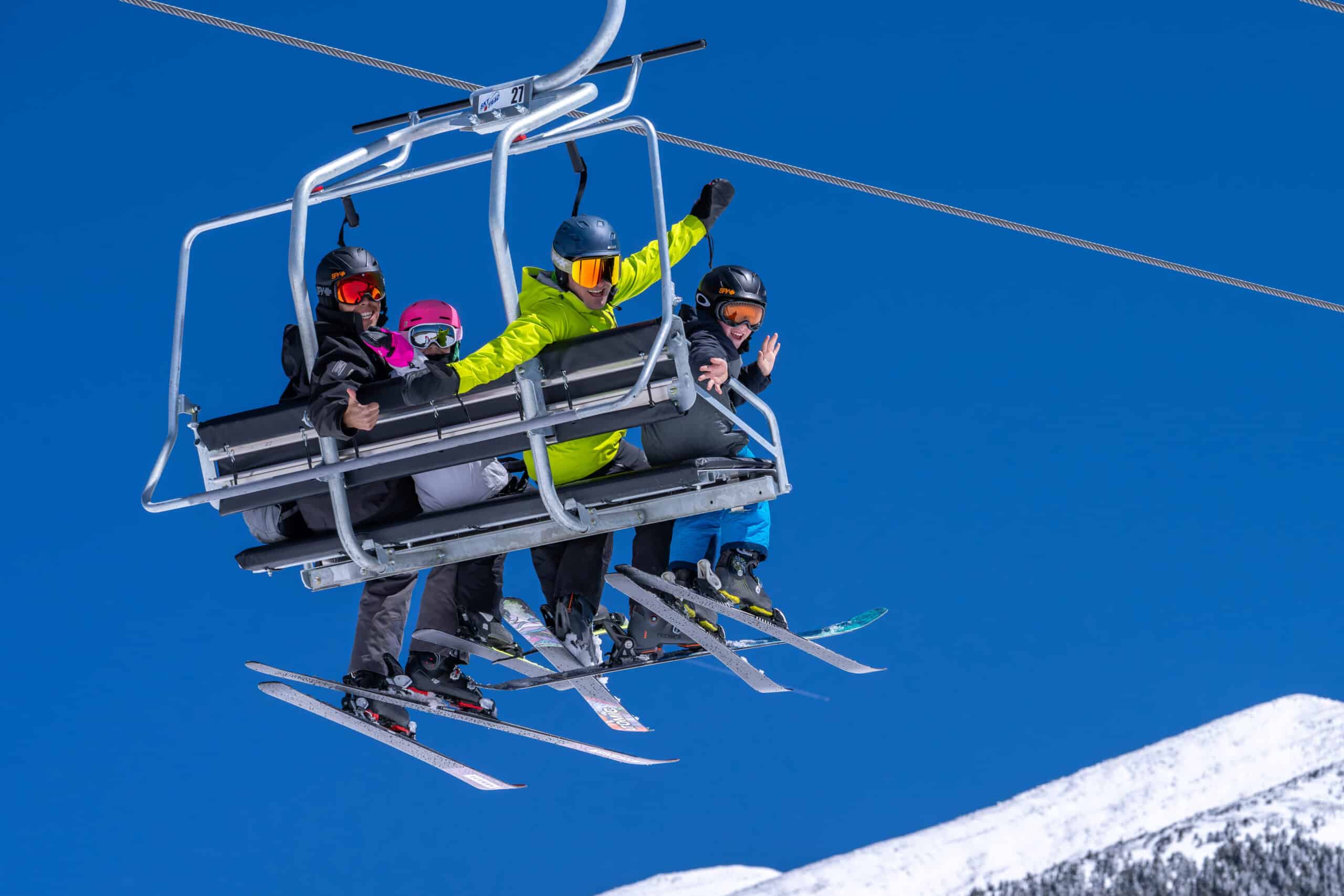 A family of 4 on Aspen Chairlift smiling and waving