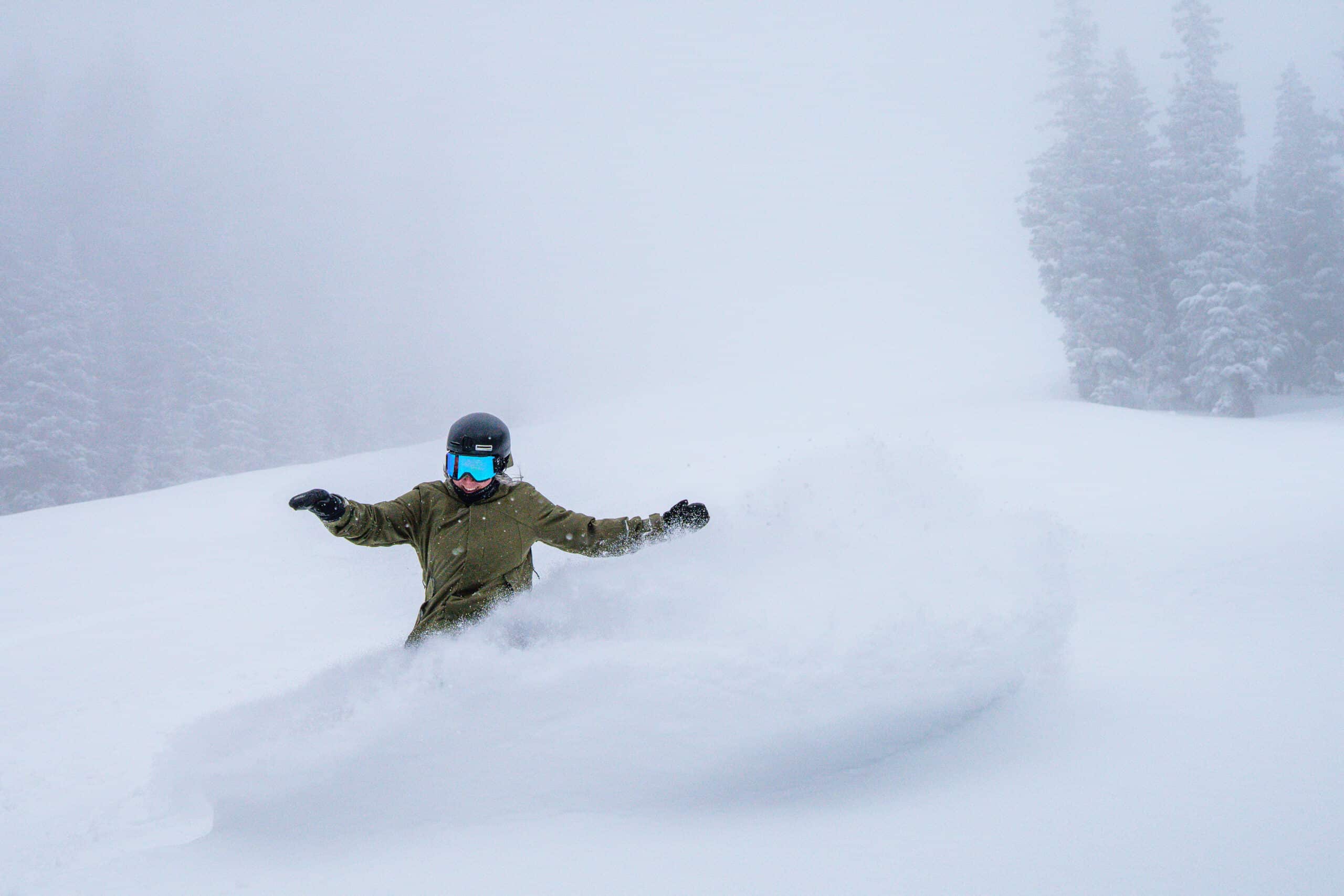 A female snowboarder slashing snow on a powder day.