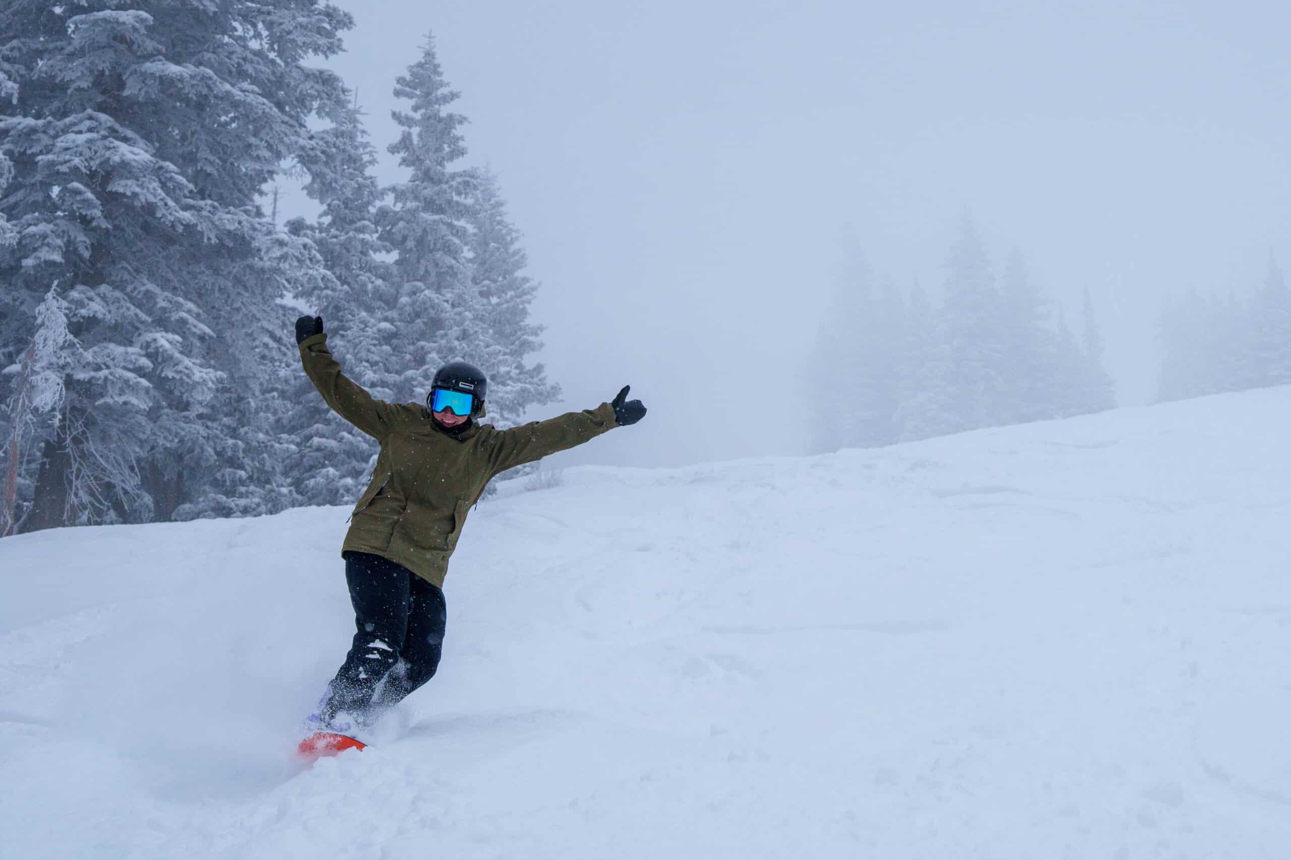Female snowboarder hands up smiling powder day
