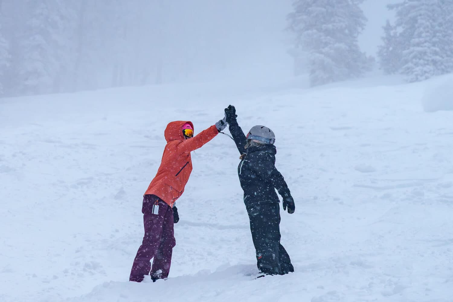 Two snowboarders high-fiving in the powder