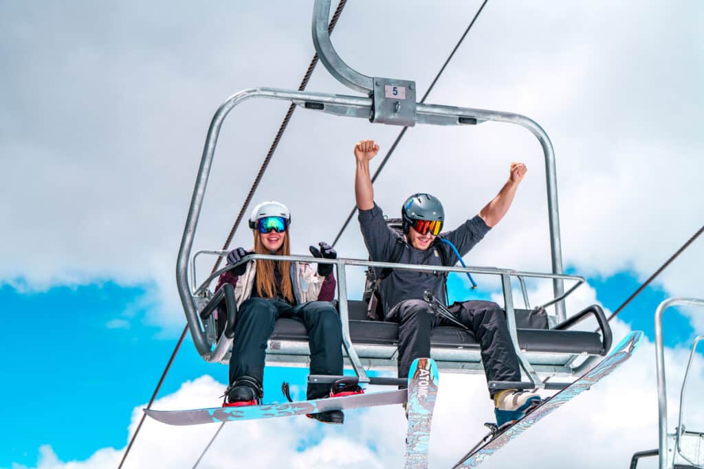 A skier and a snowboarder celebrating on the chairlift.