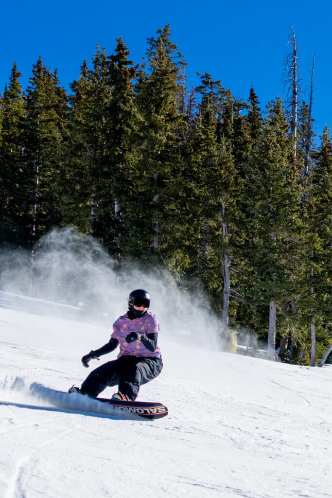 Snowboarder in a pink Hawaiian shirt carving down a run in spring conditions.