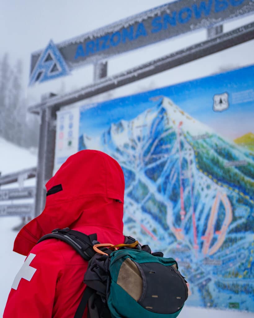 Ski Patroller with hood on standing in front of Arizona Snowbowl trail map