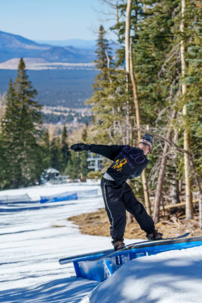 Snowboarder, from behind, wearing a beanie on a rail at the Red Tail Terrain Park