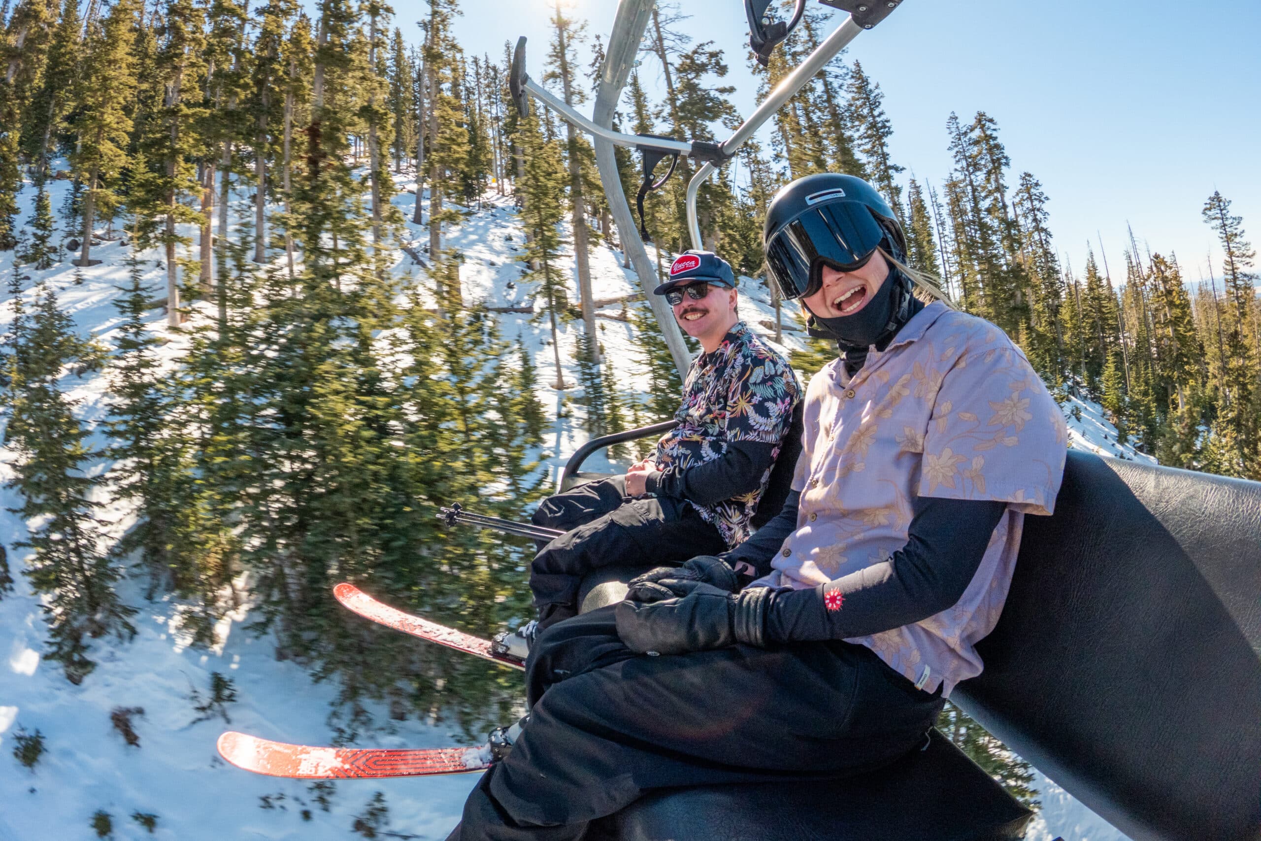 A skier and snowboarder on a chairlift at Snowbowl, wearing Hawaiian shirts