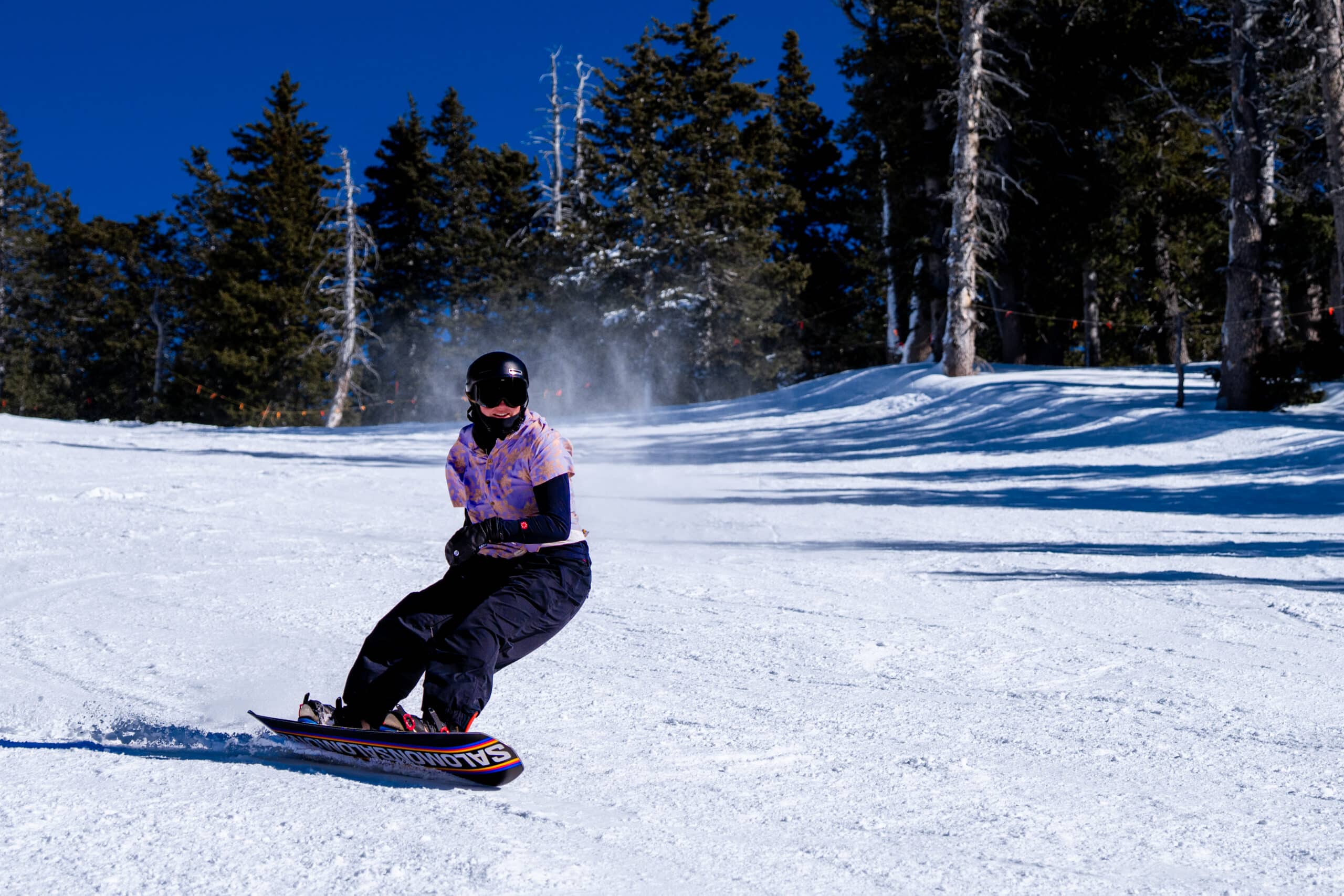 A snowboarder in a purple Hawaiian shirt coming down a run
